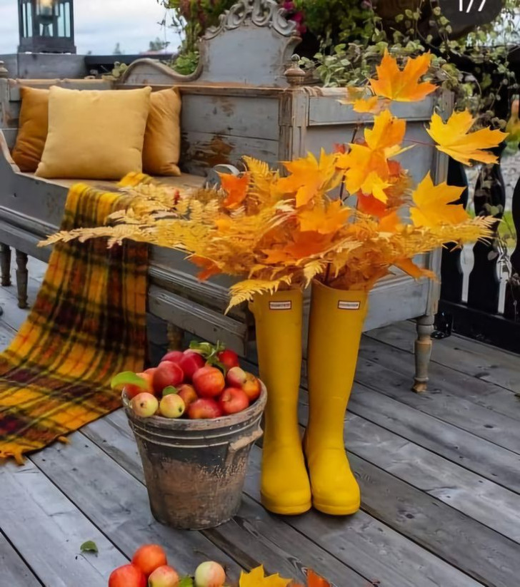 Een typische herfstdecoratie in een zithoekje buiten, met takken van gele bladeren, ton-sur-ton meubelstoffen en een emmer vol rijpe appels