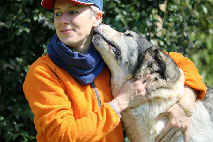 Un cane che bacia in segno di affetto la guancia di una donna che lo abbraccia