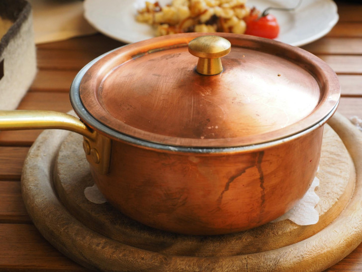 Une casserole en cuivre posée sur une planche à découper en bois dans une cuisine