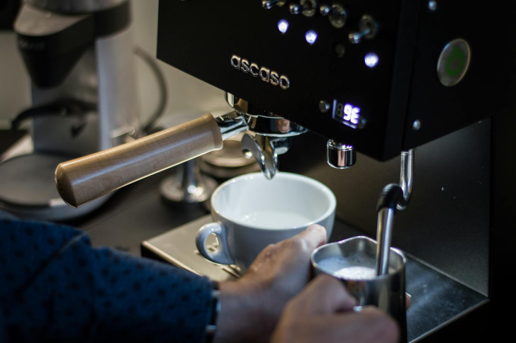 Eine Person erhitzt Milch mit einer Kaffeemaschine