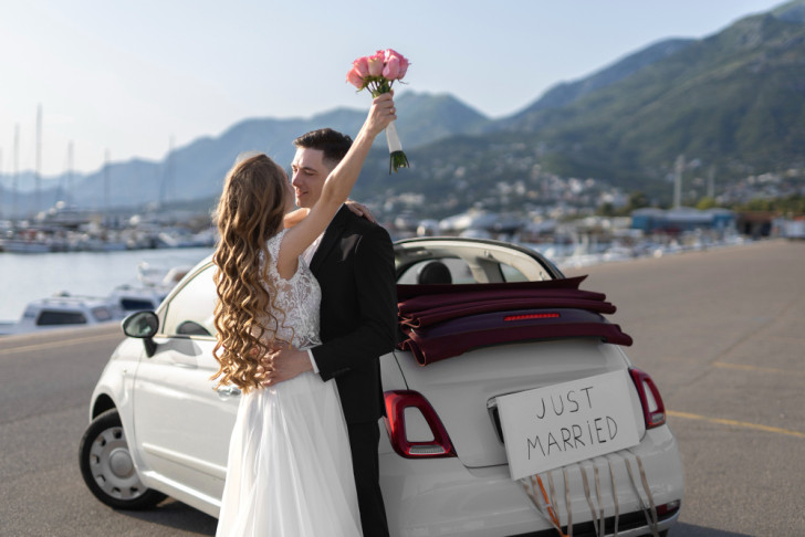 Pasgetrouwd stel omhelst elkaar voor een auto met achterop de tekst “just married”