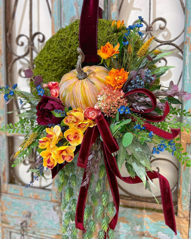 A wreath with moss, pumpkin, flowers of various colors, orchids and velvet ribbon