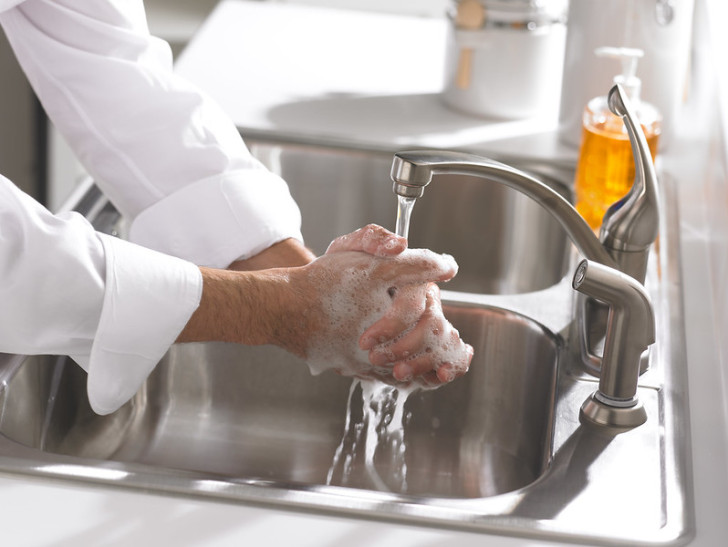 Un uomo si lava le mani con il sapone al lavandino della cucina