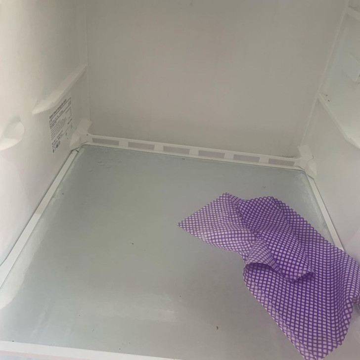 a cloth placed on the shelf of an empty fridge