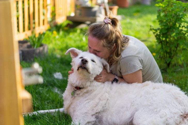 Una donna abbraccia e bacia un cane bianco in giardino