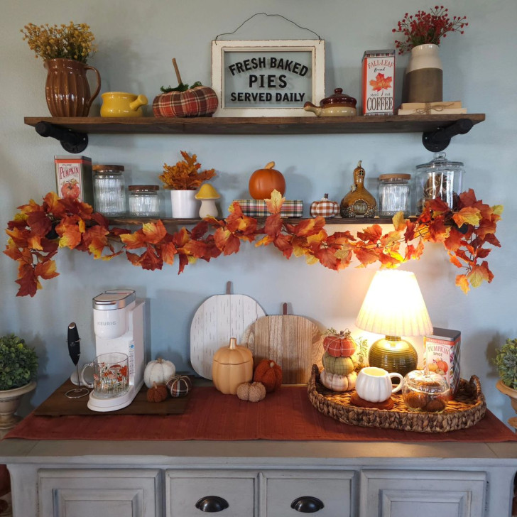 fall decorations using artificial pumpkins and leaves placed on a sideboard and the shelves above it