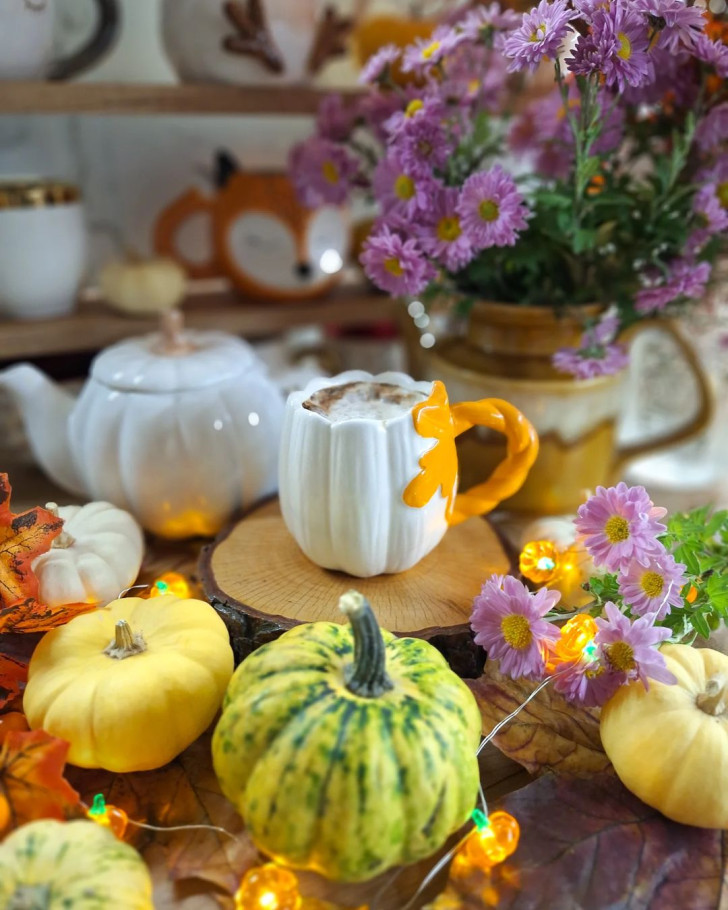 a pumpkin-shaped teacup and teapot set in the middle of a table set with fall decorations