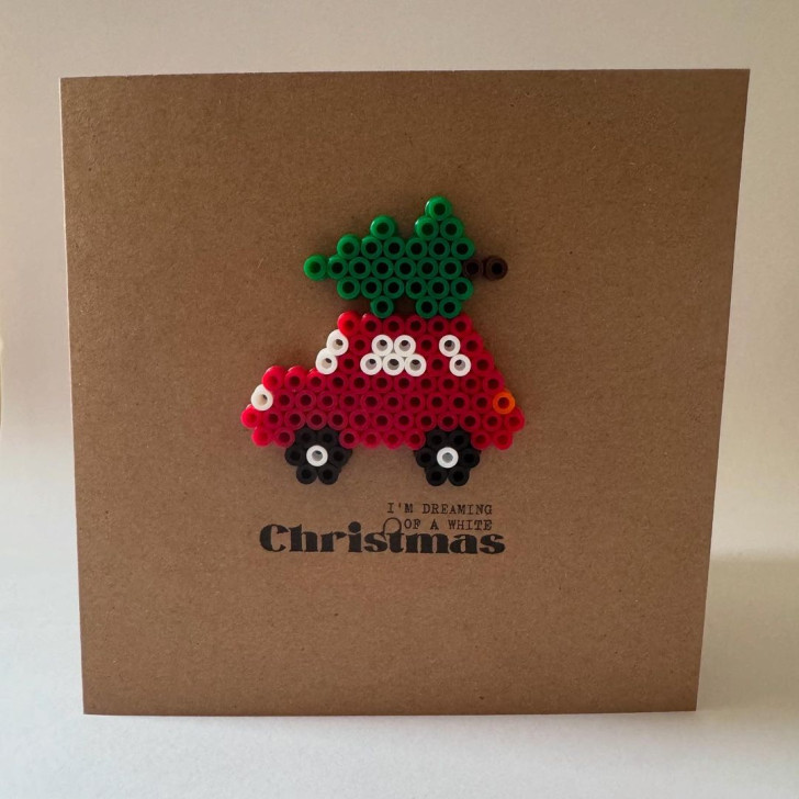 a Christmas card decorated with beads in the shape of a car carrying a tree on its roof