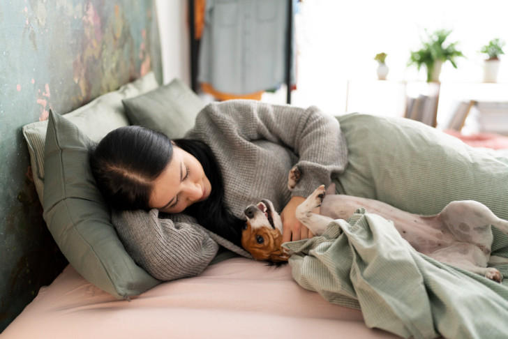 Una donna accarezza un cane a pancia in su sul letto