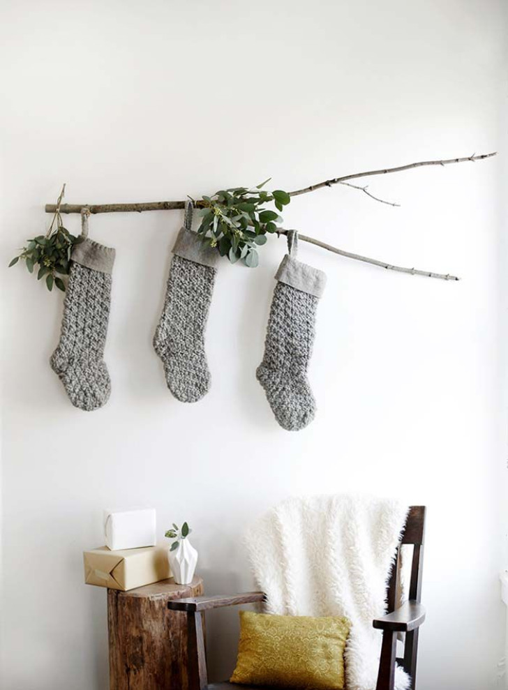 calze di natale grigie appese a un ramo su muro bianco