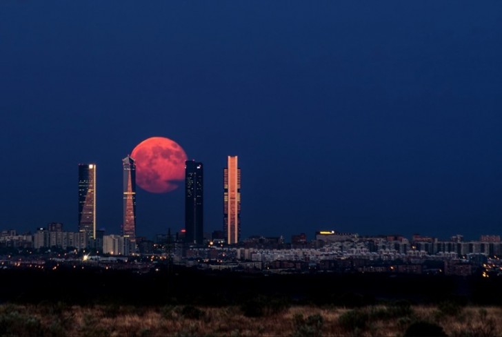 Une lune rouge gigantesque encastrée entre 2 gratte-ciel.