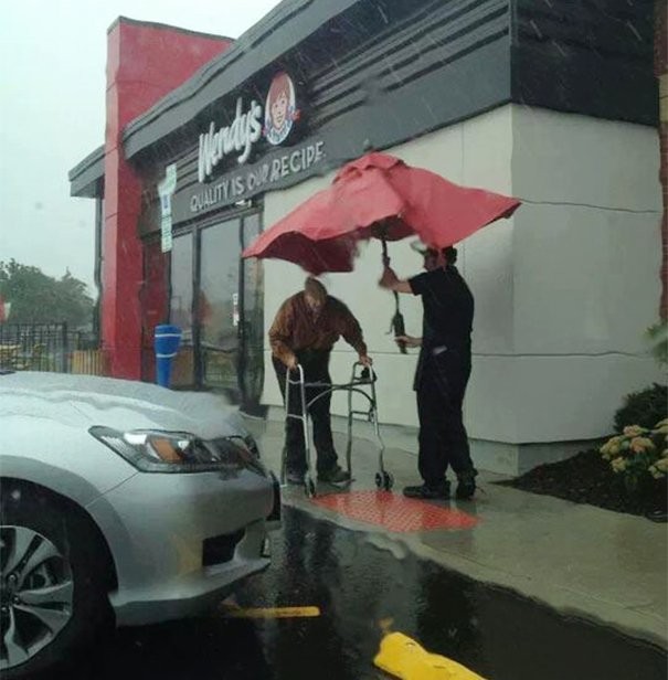 12. Il commesso di un supermercato ha usato l'ombrellone del bar per proteggere un anziano signore dalla pioggia.