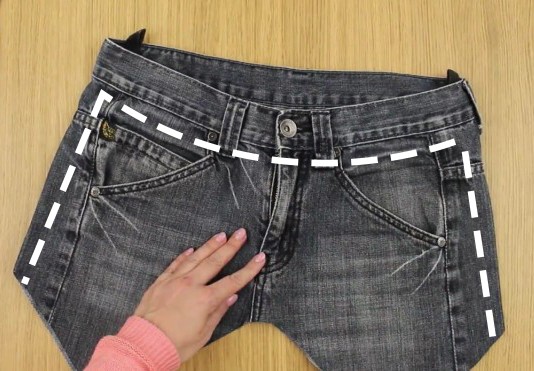 Capovolgete i jeans e partendo dal bottone ritagliate tutta la parte anteriore al di sotto della cintura, arrivando fino alle estremità laterali