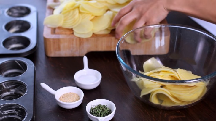 Legt die Kartoffelscheiben in eine große Schüssel und gebt erst die geschmolzene Butter, dann das Knoblauchpulver, Salz, Thymian und zuletzt Pfeffer hinzu. Vermengt es mit den Händen.
