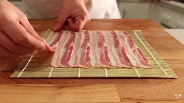 Begin by placing six slices of uncooked bacon on a sushi mat.
