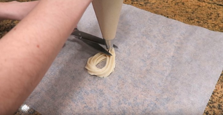 Spuit vervolgens ovalen churros op bakpapier: als je ovaal af is, kun je het deeg afknippen met een schaar.