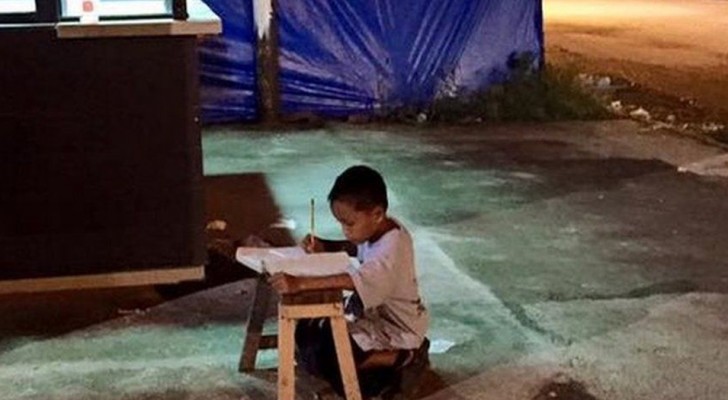 En 9-årig pojke gör sina läxor på gatan under en reklamskylt eftersom han inte har någon el hemma och är fattig