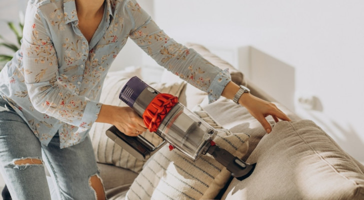 vrouw die een bank schoonmaakt met een stofzuiger