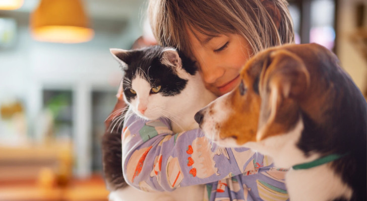 Una bimba felice mentre abbraccia un gatto e sta accanto a un cane