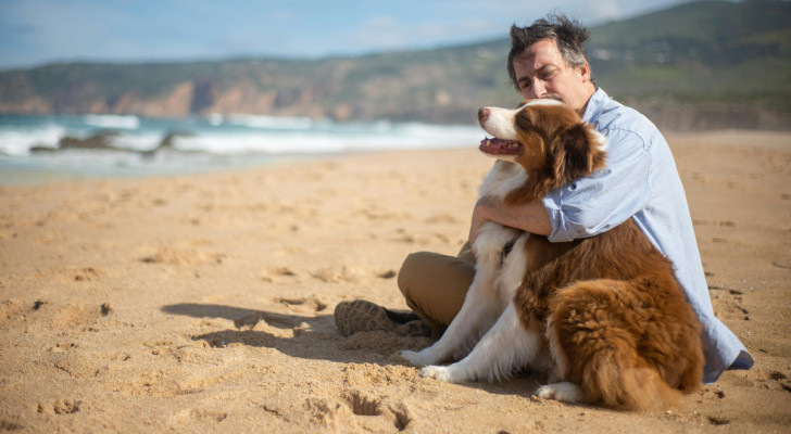 Un uomo abbraccia un cane seduti sulla riva del mare