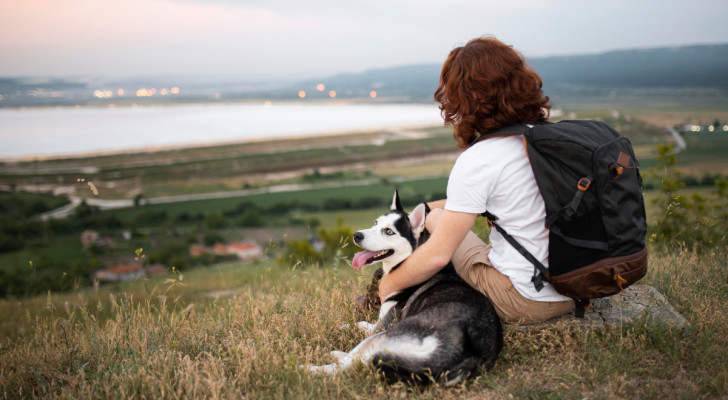 un cane sdraiato accanto a un uomo che lo abbraccia mentre guarda un panorama