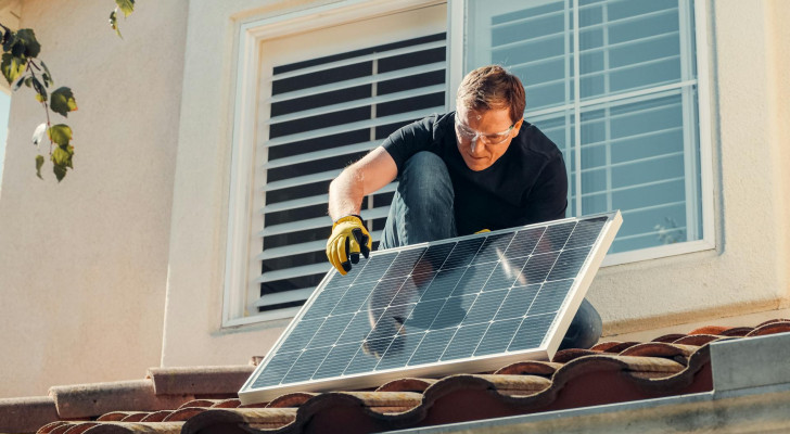 A man installs a small photovoltaic panel on a rooftop