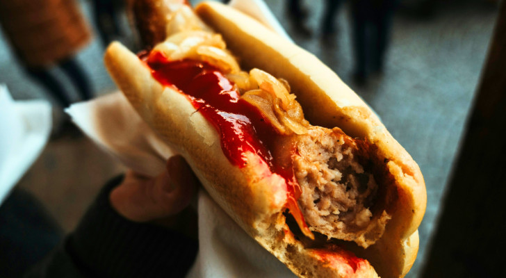 Eine Hand, die einen Hot Dog mit Ketchup schüttelt und bereit ist, eine schnelle und leckere Mahlzeit zu genießen