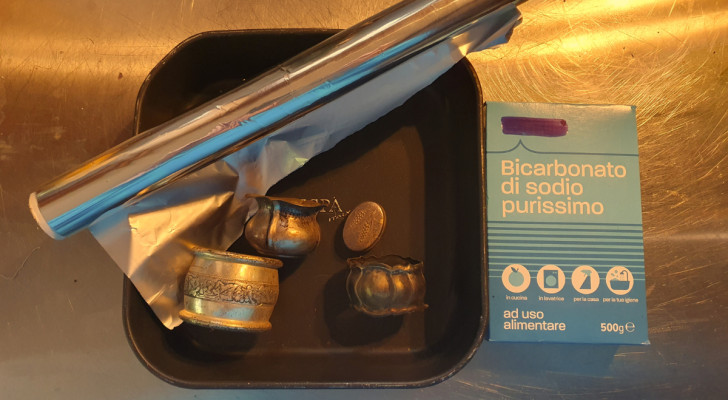 förstörda silverföremål på en bricka med en rulle aluminiumfolie och ett paket natriumbikarbonat