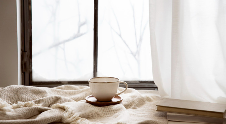 looking out a window on a winter day, with a blanket and a hot drink on the sill