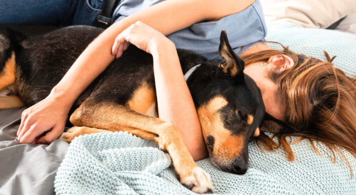 Una donna abbraccia un cane addormentato sul letto